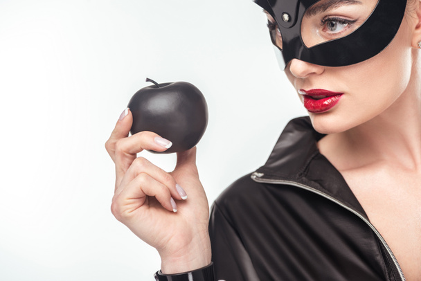 Verleidelijke jonge vrouw in masker houden zwarte appel geïsoleerd op wit - Foto, afbeelding