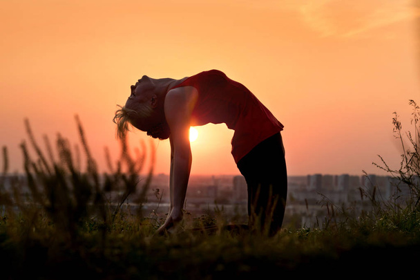 A woman does yoga in nature. Silhouette in sunset. Ushtrasana - camel pose - Foto, imagen