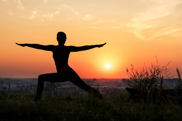A woman does yoga in nature. Silhouette in sunset. Virabhadrasana - warrior pose - Fotografie, Obrázek