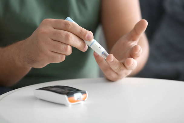 Diabetic man taking blood sample with lancet pen at home, closeup - Photo, image