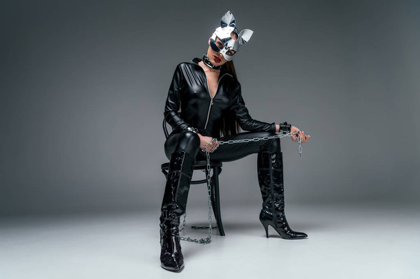 Kinky woman in sexy costume sitting on chair and holding chain on grey background - Fotografie, Obrázek