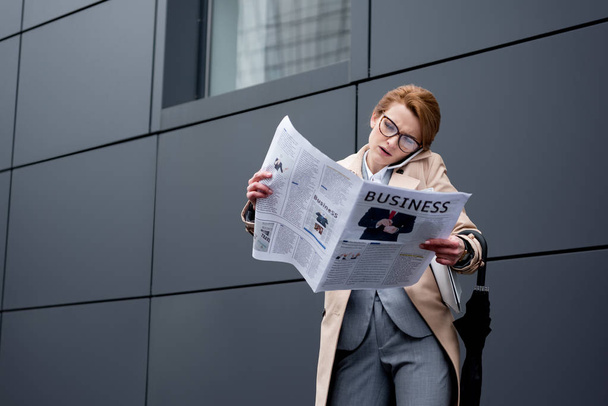 zakenvrouw praten over smartphone tijdens het lezen van de krant op straat - Foto, afbeelding