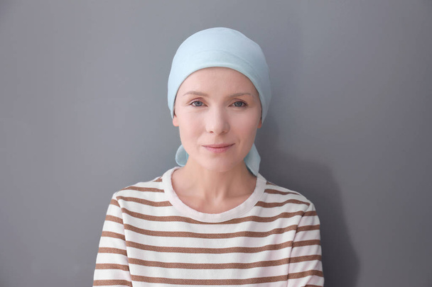 Young woman with cancer in headscarf on grey background - Foto, imagen