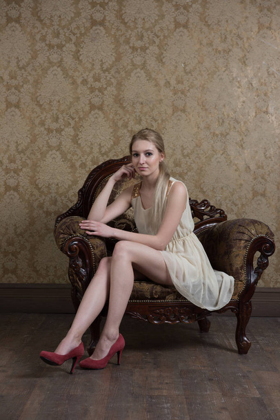 fiatal gyönyörű lány pózol stúdió, vintage szék, fehér ruhás ülő - Fotó, kép