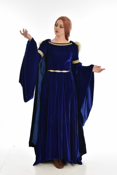 Ganzkörperporträt einer Frau mit langen Haaren, die ein blaues mittelalterliches Samtkleid und einen Pelzmantel trägt. Stehende Pose, isoliert auf weißem Hintergrund. - Foto, Bild