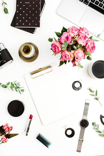 Female home office workspace with clipboard, laptop, rose flowers, eucalyptus branches, fashion accessories and cosmetics. Flat lay, top view fashion mockup this space for text. - Photo, Image