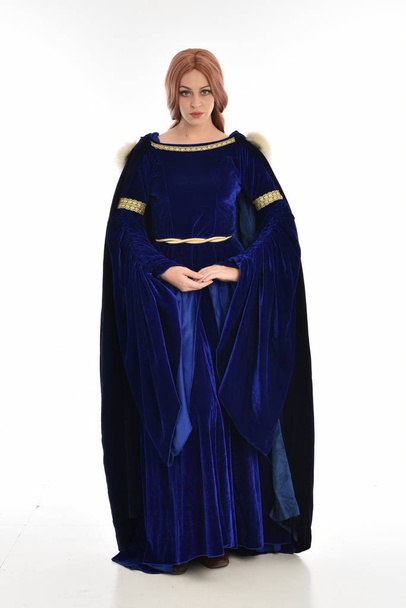 retrato de comprimento total da mulher com cabelos longos, vestindo um vestido medieval de veludo azul e capa de pele. postura em pé, isolada sobre fundo branco
. - Foto, Imagem