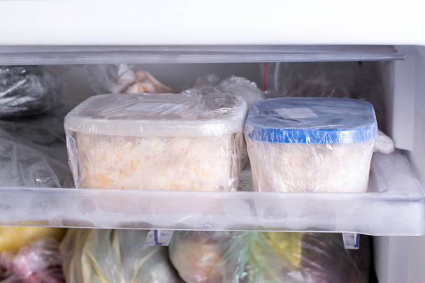 Un recipiente con comida en el congelador. Un congelador lleno de pollo, sopa y varios alimentos congelados
 - Foto, Imagen