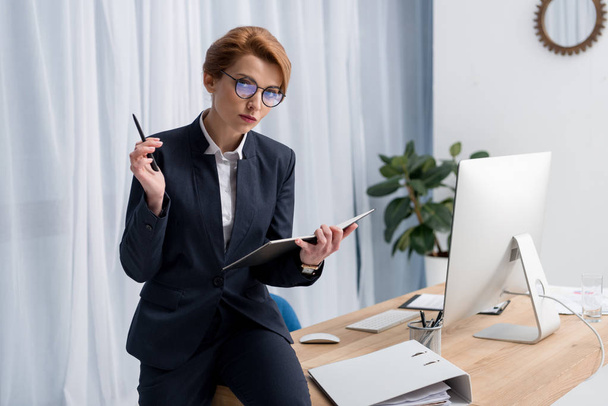 portrait of businesswoman in eyeglasses with notebook at workplace in office - Foto, imagen