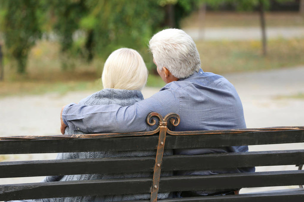 Mature couple sitting on bench outdoors - 写真・画像