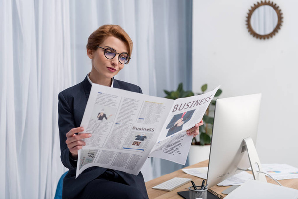portrait of businesswoman in eyeglasses reading newspaper at workplace in office - Fotó, kép
