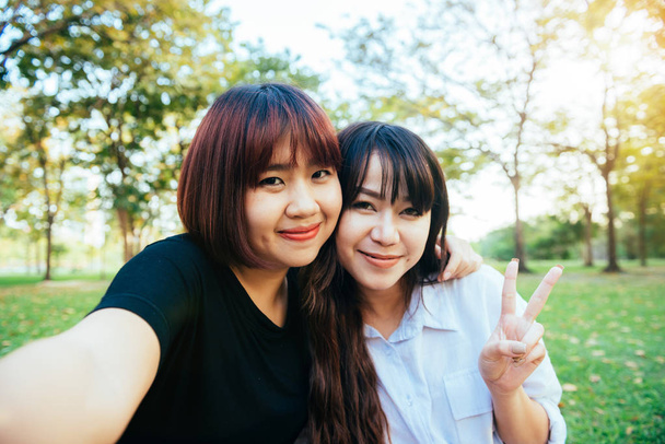 Dva krásné šťastné mladé asijské ženy přátelé baví spolu v parku a užívat si selfie. Happy bokovky mladé asijské dívky s úsměvem a při pohledu na fotoaparát. Životní styl a přátelství pojmy. - Fotografie, Obrázek