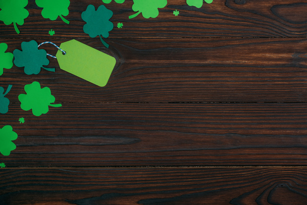 top view of blank green label and shamrocks on wooden table - Foto, Bild