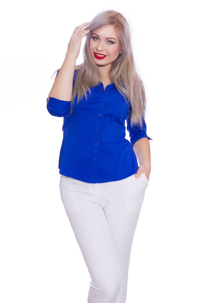 Studio business portrait of a young blonde woman in a dark blue shirt and white trousers. Girl posing on isolated white background. Smiling, looking at the camera - Fotoğraf, Görsel