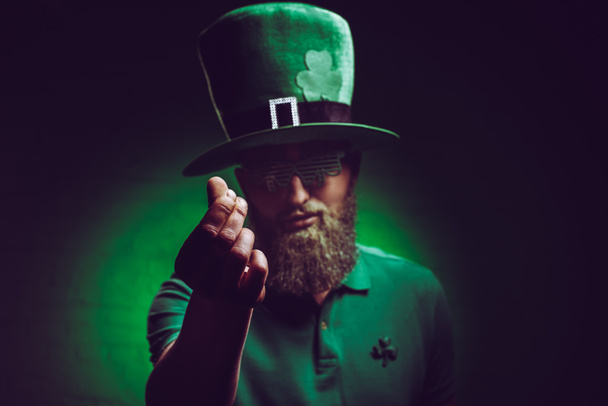 アイルランドの緑の帽子とカメラで身振りで示す面白いメガネのひげを生やした若い男 - 写真・画像