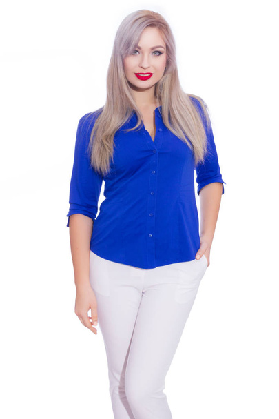 Studio business portrait of a young blonde woman in a dark blue shirt and white trousers. Girl posing on isolated white background. Smiling, looking at the camera - Photo, image