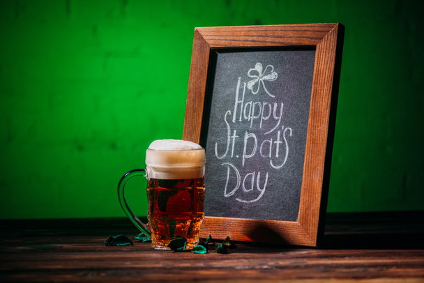 marco de madera con feliz día de San Patricio inscripción y vaso de cerveza en la mesa
 - Foto, Imagen
