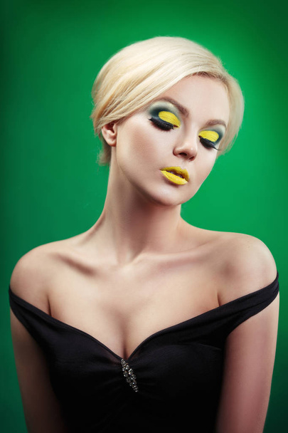 beauty portrait of beautiful blonde woman in sexy evening black dress with yellow makeup looking down on green background  - Fotografie, Obrázek