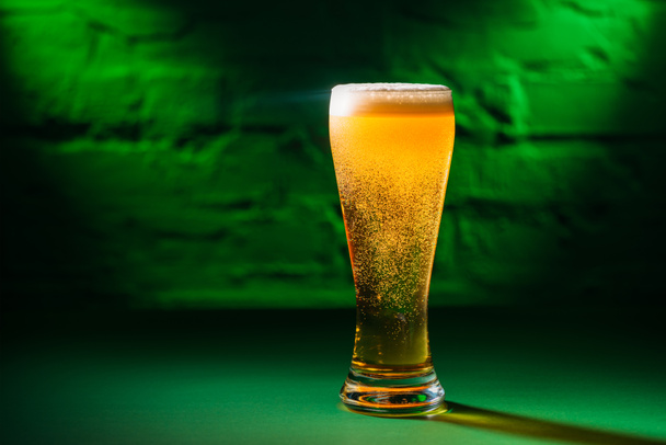 Nahaufnahme von Glas mit frischem, kaltem, bernsteinfarbenem Bier in grünem Licht, Konzept zum Heiligen Patricks Day - Foto, Bild