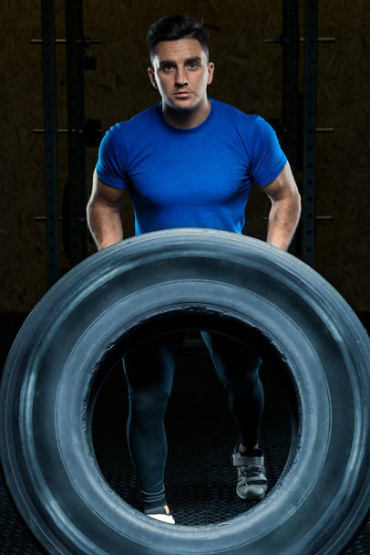 портрет сильного спортсмена с большим тяжелым колесом в тренажерном зале
 - Фото, изображение