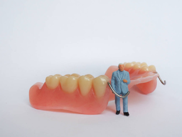 Miniature elderly standing on removable denture, on white backgr - Photo, image