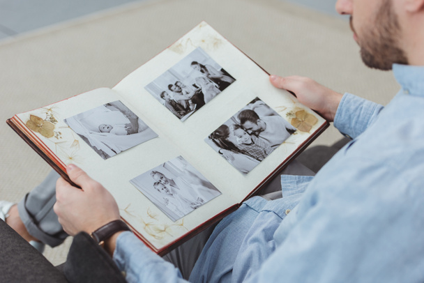 Teilansicht eines Mannes mit Fotoalbum in den Händen, der zu Hause auf dem Sofa ruht - Foto, Bild