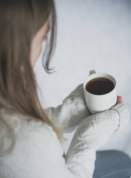 Bir omuz Pov görüntü oturan ve beyaz zemin üzerine siyah kahve bir fincan sıcak tutarak ve üzgün ve yalnız arayan genç bir kızın üzerinde. - Fotoğraf, Görsel