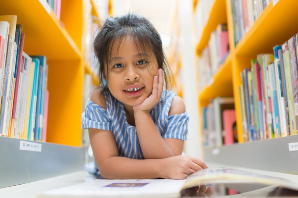 Азиатская милая девушка, улыбающаяся в библиотеке на размытой книжной спинке
 - Фото, изображение