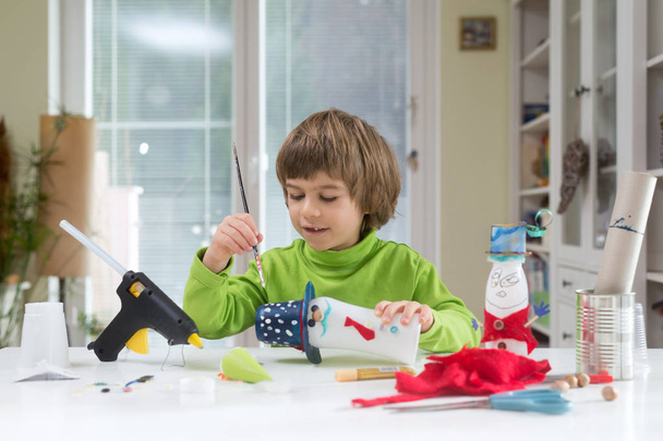 Μικρό αγόρι είναι δημιουργική ζωγραφική κουκίδες στο σπιτικό do-it-yourself παιχνίδια κατασκευασμένα από γιαούρτι μπουκάλι και χαρτί. Δικαιολογητικά δημιουργικότητα, εκμάθηση μέσω της πράξης, τέχνης το χέρι. Δημιουργική ψυχαγωγία για τα παιδιά σε εσωτερικούς χώρους. - Φωτογραφία, εικόνα