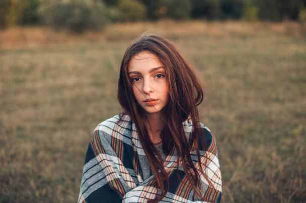 young woman with plaid on shoulders sitting on field  - Fotografie, Obrázek