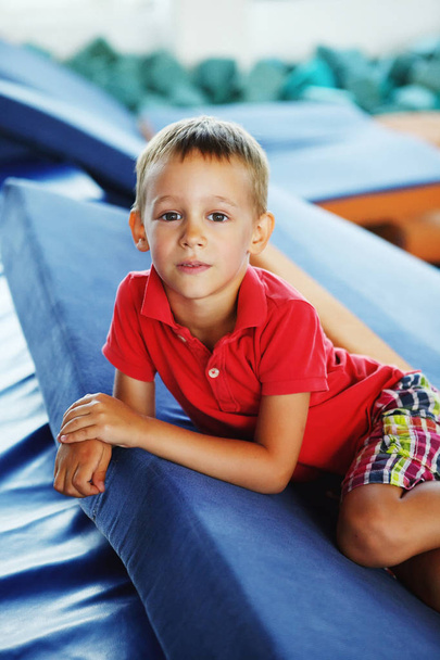 Un chico con una camiseta roja y pantalones cortos en un trampolín en el gimnasio
 - Foto, Imagen