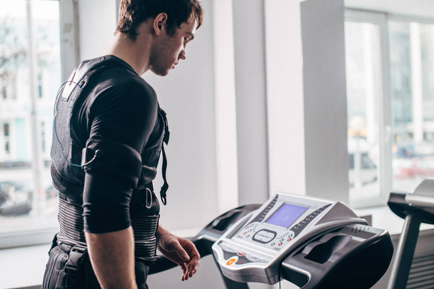 Man in black suit for ems training running on treadmill at gym - 写真・画像