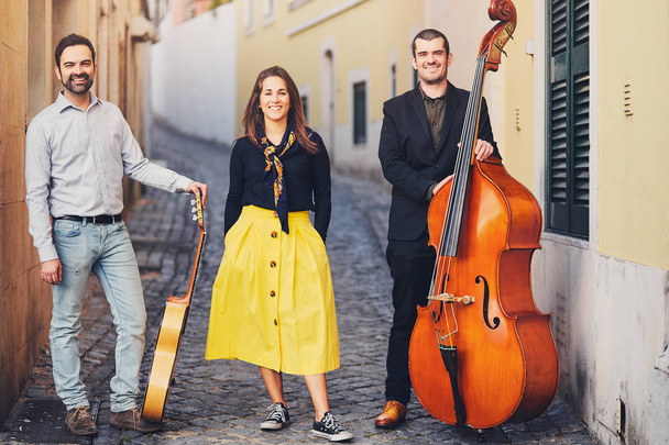 Ένα μουσικό συγκρότημα από τρία άτομα σε ένα παλιό ευρωπαϊκό δρόμο. Το συγκρότημα αποτελείται από δύο άνδρες και ένα κορίτσι. Άνδρες με ένα διπλό μπάσο και την κιθάρα. Αντισυμβατικό δημιουργικούς ανθρώπους με μουσικά όργανα. - Φωτογραφία, εικόνα