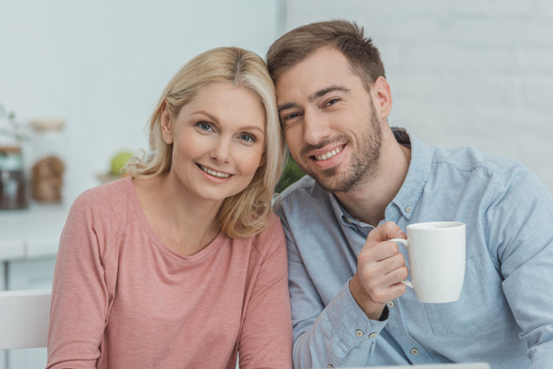portrait of smiling mother and grown son with cup of coffee looking at camera - Fotografie, Obrázek