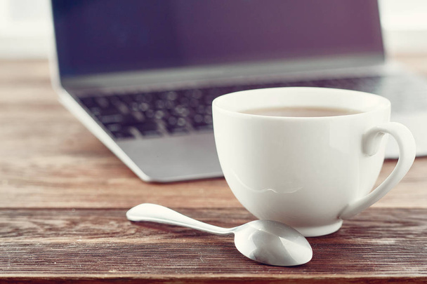 Bir fincan çay ile ahşap masa, sığ derinliği alan, seçici odak üstünde laptop - Fotoğraf, Görsel