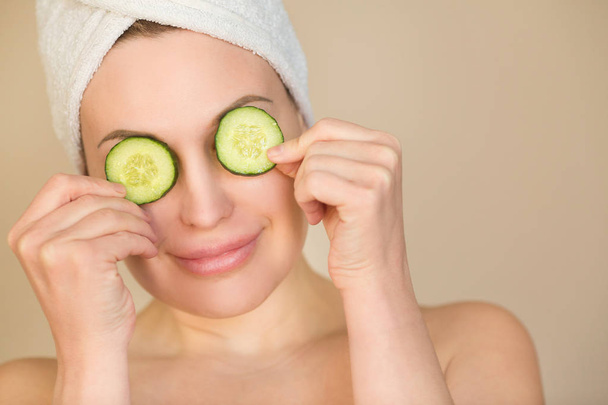 portrait of a beautiful young girl with a towel on her head with cucumber slices in her hands - 写真・画像