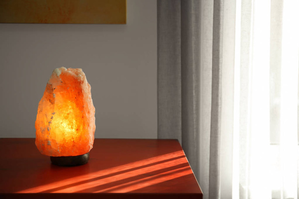 Himalayan salt lamp on wooden cabinet indoors - Foto, Imagen