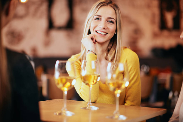 Portrait of young beautiful blonde woman in the bar. Glasses of wine in front of her. - Foto, imagen
