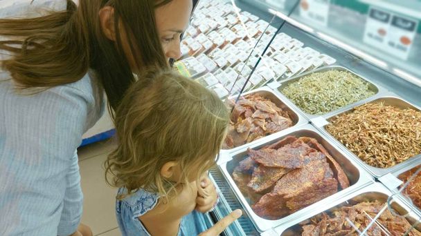 Junge Mutter mit kleiner Tochter wählt Fertiggericht im Supermarkt - Foto, Bild
