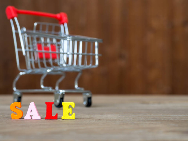 Colorful wooden word SALE on wooden table and shopping cart and background wooden. English alphabet made of wooden letter color. The concept of shopping and Discount festival - Zdjęcie, obraz