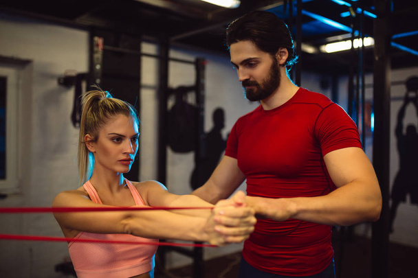 Young woman exercising at gym with male personal trainer. - Photo, Image
