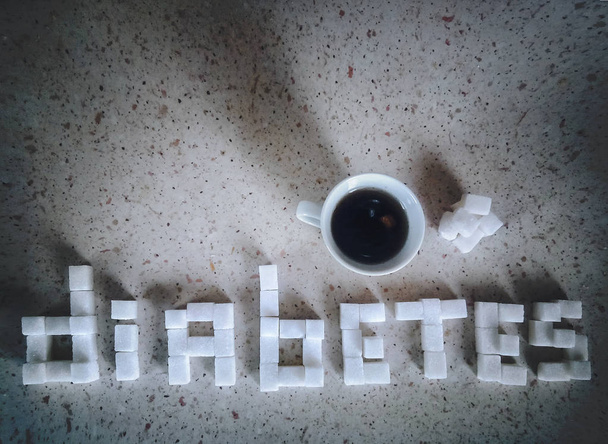 Word diabetes made up of cubes of sugar. Concept of diabetes. Cup of coffee on the table. - Fotografie, Obrázek