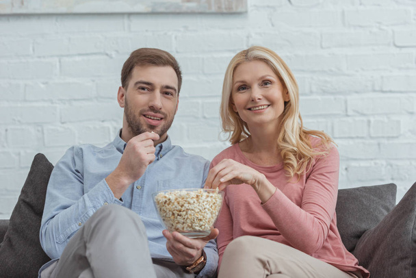 portrait of smiling mother and son eating popcorn together while watching film at home - Photo, image
