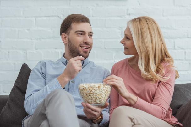 portrait of smiling mother and son eating popcorn together while watching film at home - Fotoğraf, Görsel