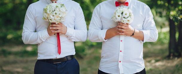 Deux jeunes hommes en chemises blanches tiennent dans leurs mains des bouquets de fleurs blanches
 - Photo, image