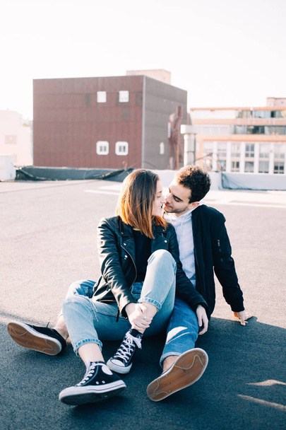 Stylish and trendy hip hipsters millennials couple, boyfriend and girlfriend sit on top of rooftop at sunset, look at each other fondly. Concept relationship goals of new generation, bloggers style - Photo, image