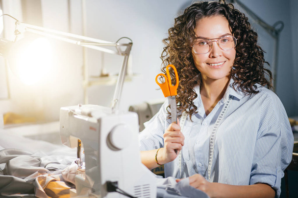 caucasian dressmaker holding orange scissors while working at studio - Фото, зображення
