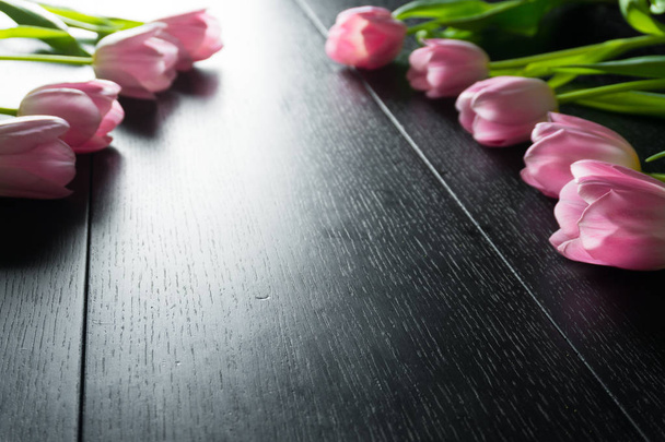 Border from bright pink tulips flowers on black wooden background. - Photo, Image