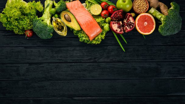 Healthy food. Fish salmon, avocado, broccoli, fresh vegetables, nuts and fruits. On a black background. Top view. Copy space. - 写真・画像