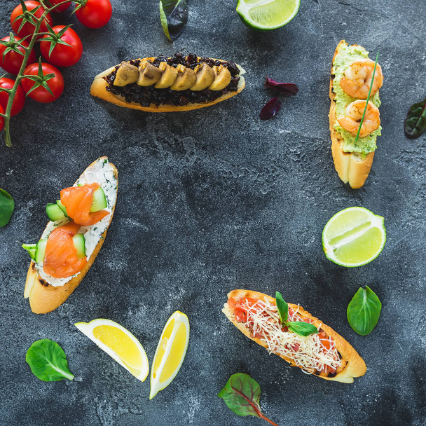 Sandwiches with prawns, salmon, mushrooms and limes on dark background. Restaurant food  - Фото, изображение